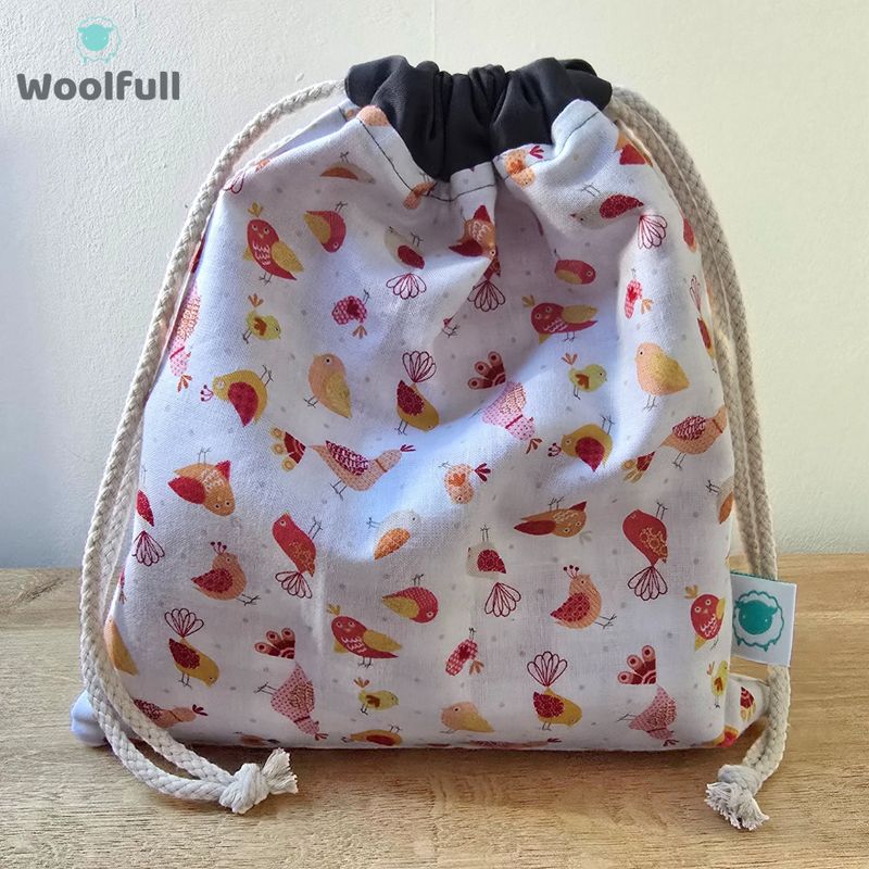 A drawstring bag in a white fabric with red and yellow cartoon birds.