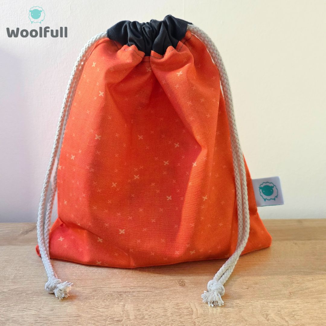 A drawstring bag in an orange fabric with small crosses.