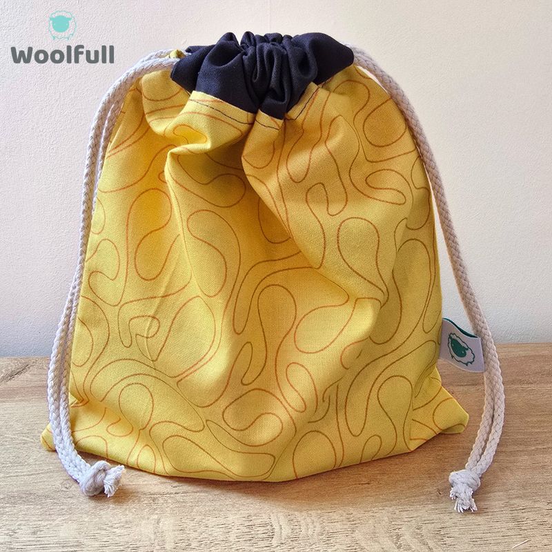A drawstring bag in a yellow fabric with orange swirls.