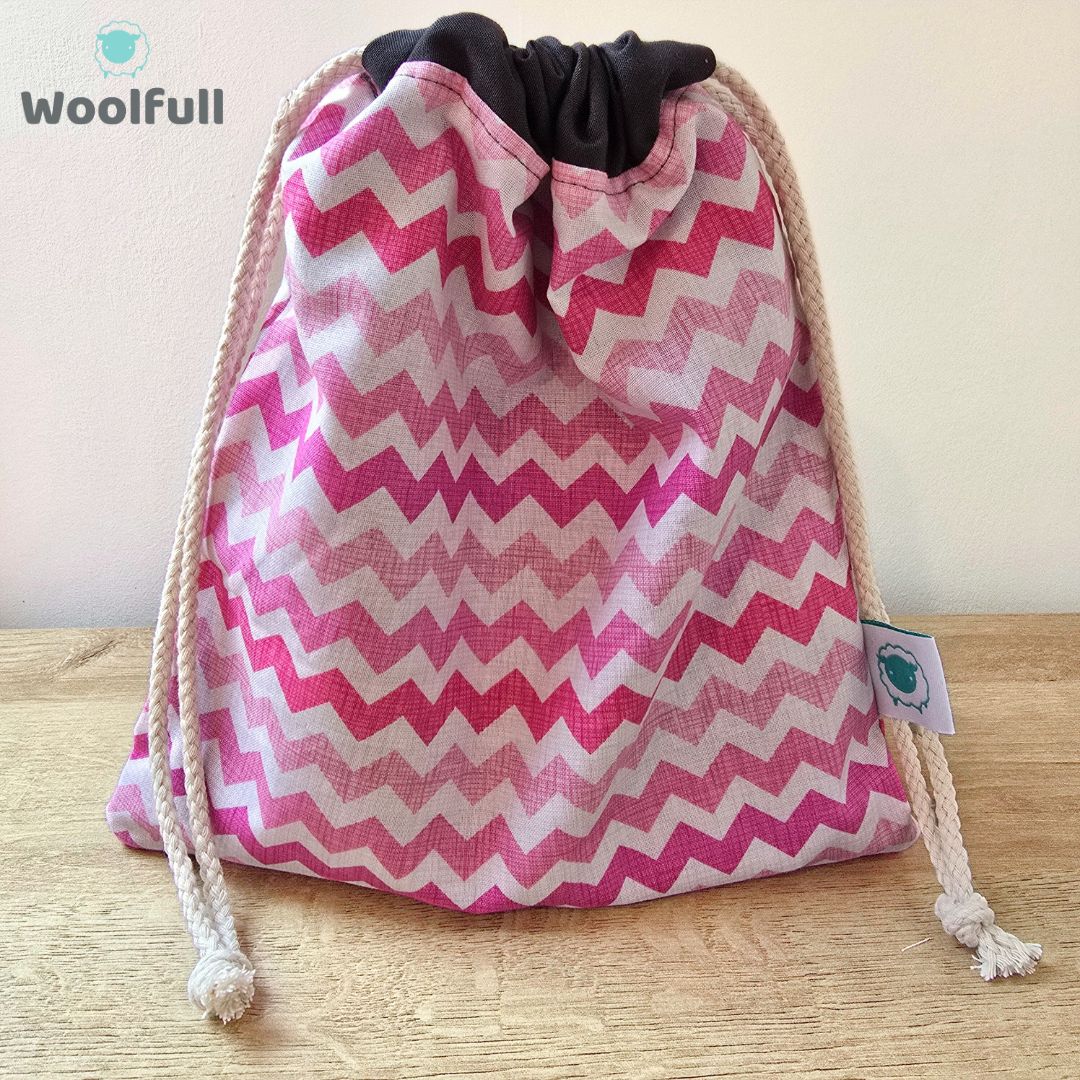 A drawstring bag in a white and pink zig zag fabric.