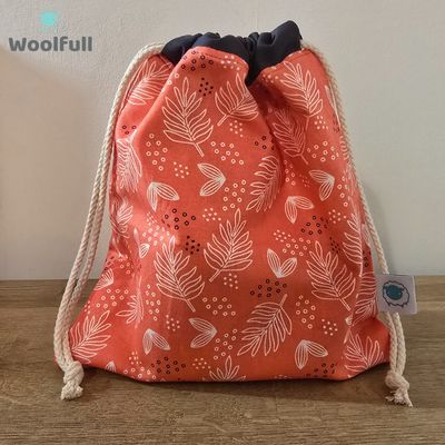 A drawstring bag in a coral fabric with white leaves.