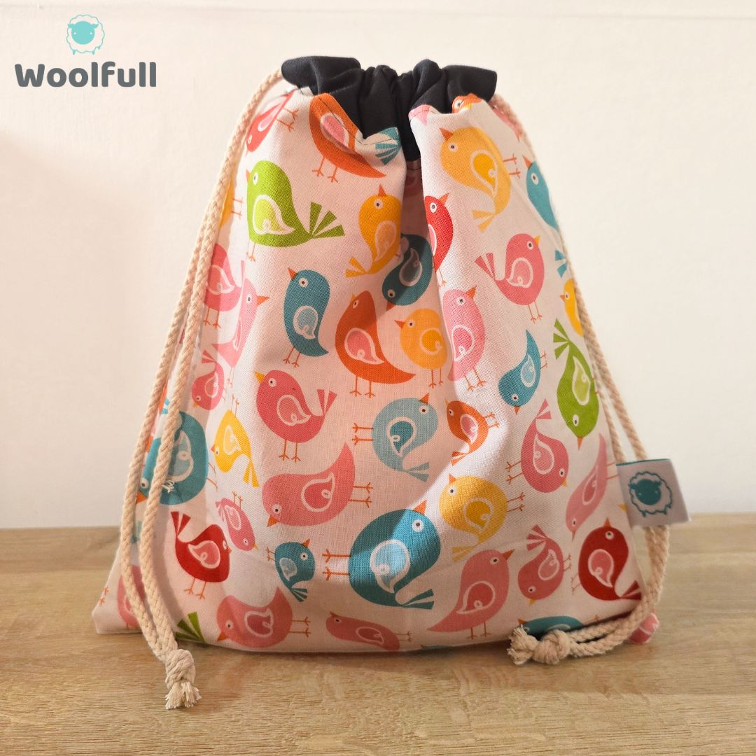A drawstring bag in a white fabric with multicoloured cartoon birds.