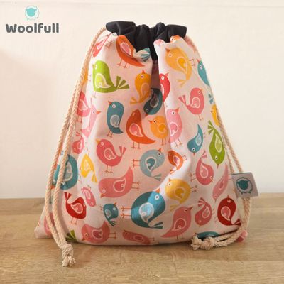 A drawstring bag in a white fabric with multicoloured cartoon birds.