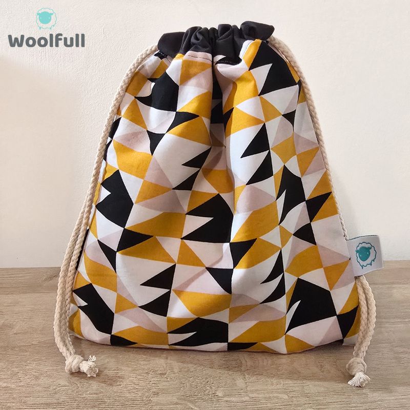 A drawstring bag in a white fabric with mustard, grey and black triangles.