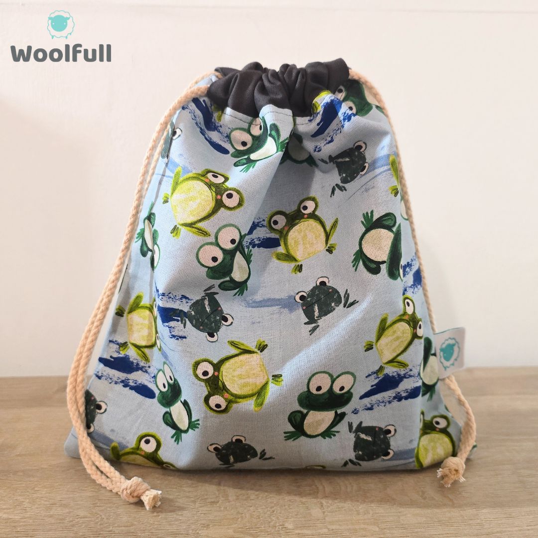A drawstring bag in a blue fabric with green frogs.