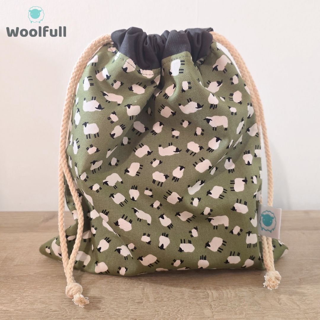 A drawstring bag in a green fabric with white sheep.