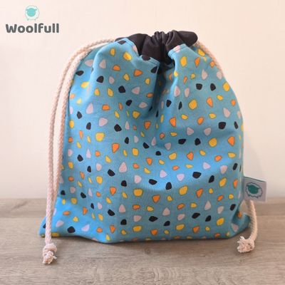 A drawstring bag in a blue fabric with orange, yellow and grey pebble shapes.