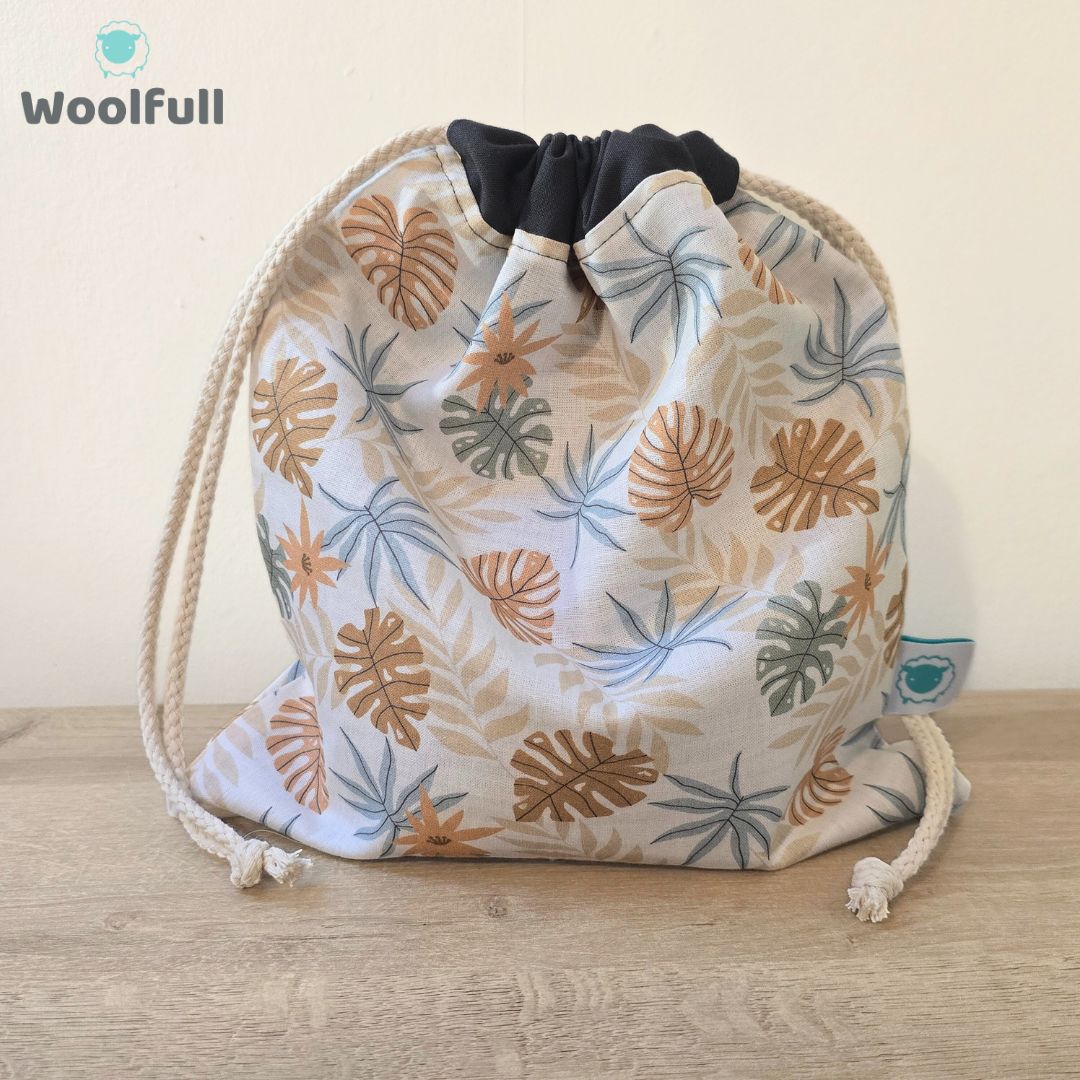 A drawstring bag in a white fabric with brown and blue leaves.