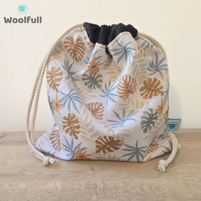 A drawstring bag in a white fabric with brown and blue leaves.
