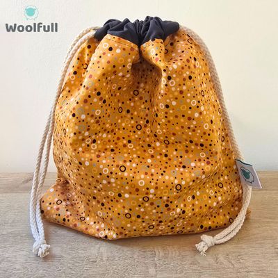 A drawstring bag in an orange fabric with multicoloured spots.