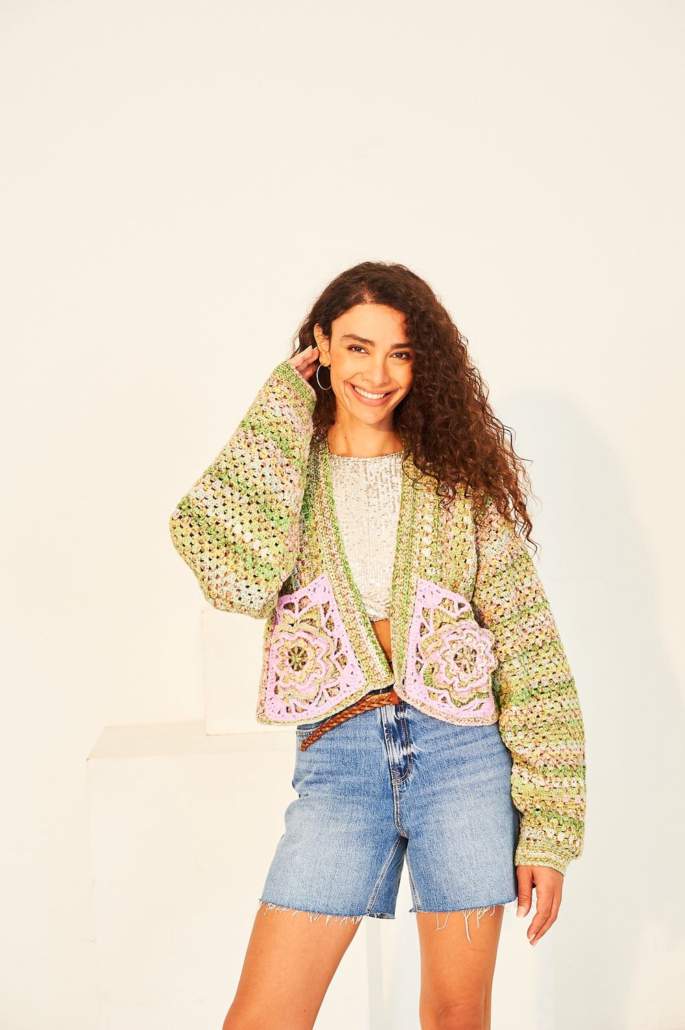 A woman is wearing a variegated green and pink short crocheted jacket.