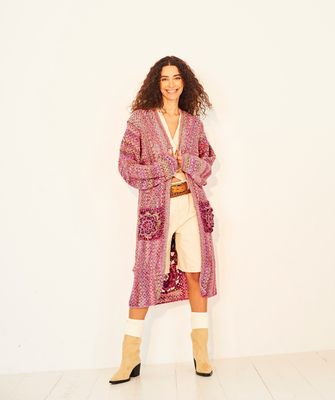 A woman is wearing a variegated pink and green long crocheted jacket.