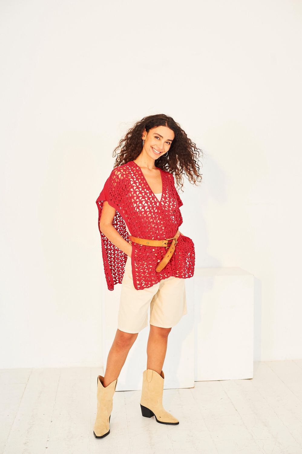 A woman is wearing a red crocheted beach cover up.