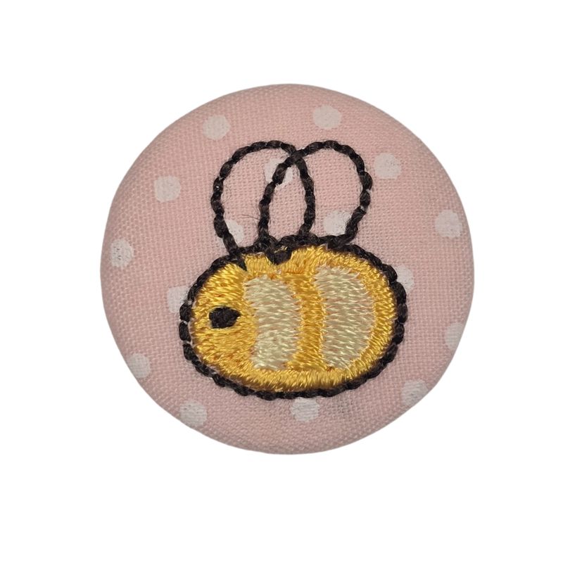 A round, pink fabric covered button with an embroidered bee.
