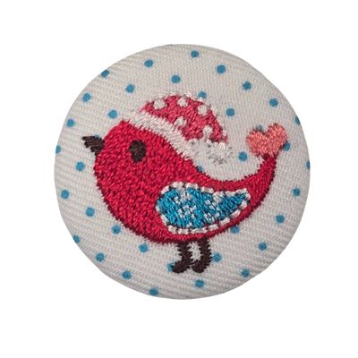 A round, white fabric covered button with a red embroidered bird.