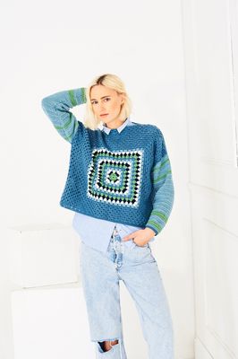 A woman is wearing a crocheted sweater in shades of blue.