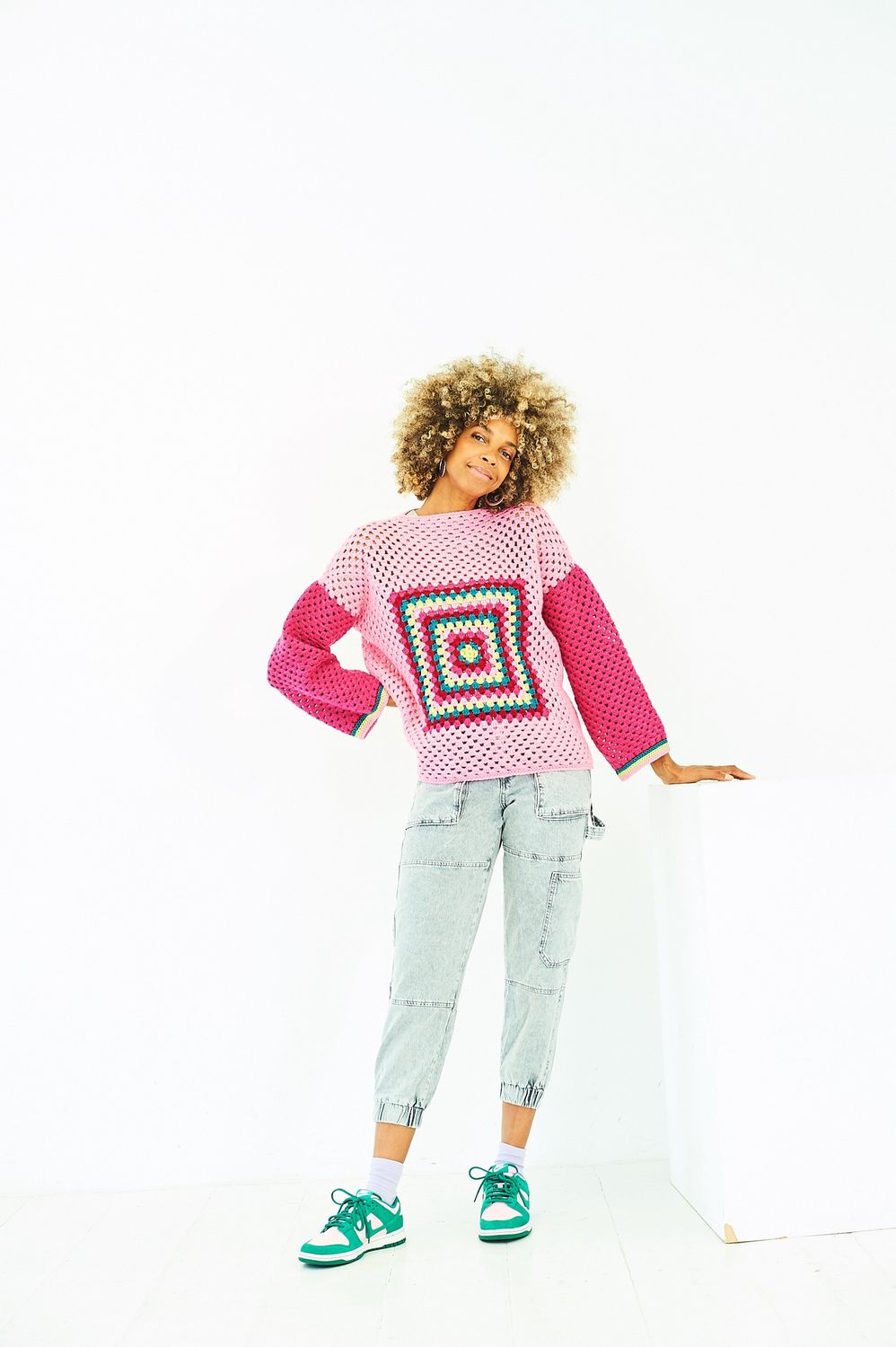 A woman is wearing a crocheted sweater in shades of pink.
