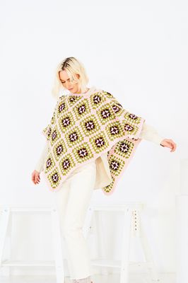 A woman is wearing a crocheted poncho in shades of pink, green and dark purple.
