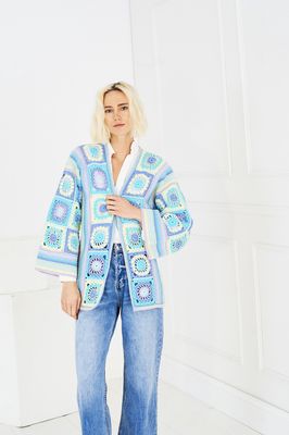 A woman is wearing a crocheted jacket in shades of blue and green.