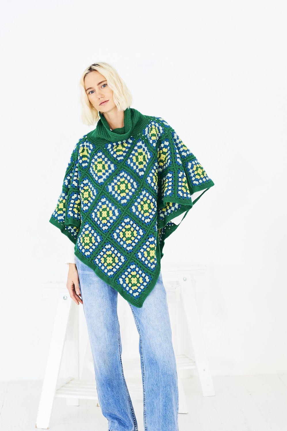 A woman is wearing a crocheted poncho in shades of blue and dark green.