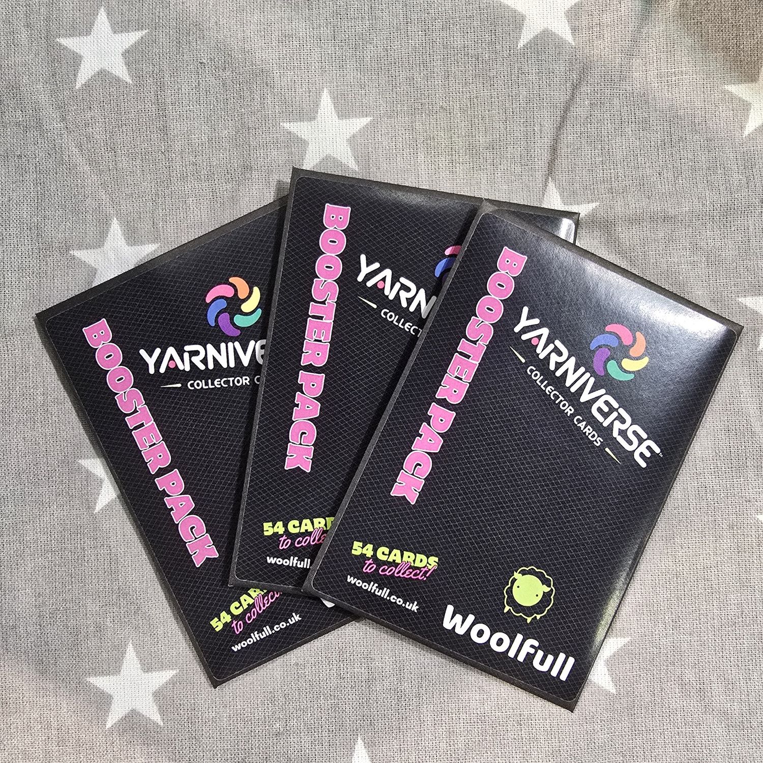 3 Yarniverse envelopes laid on a grey fabric background.