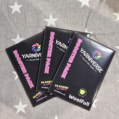 3 Yarniverse envelopes laid on a grey fabric background.
