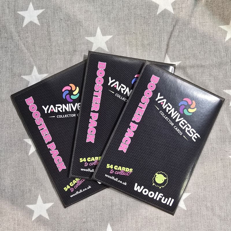 3 Yarniverse envelopes laid on a grey fabric background.