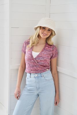 A woman is wearing a variegated pink, short sleeved knitted ballet cardigan.