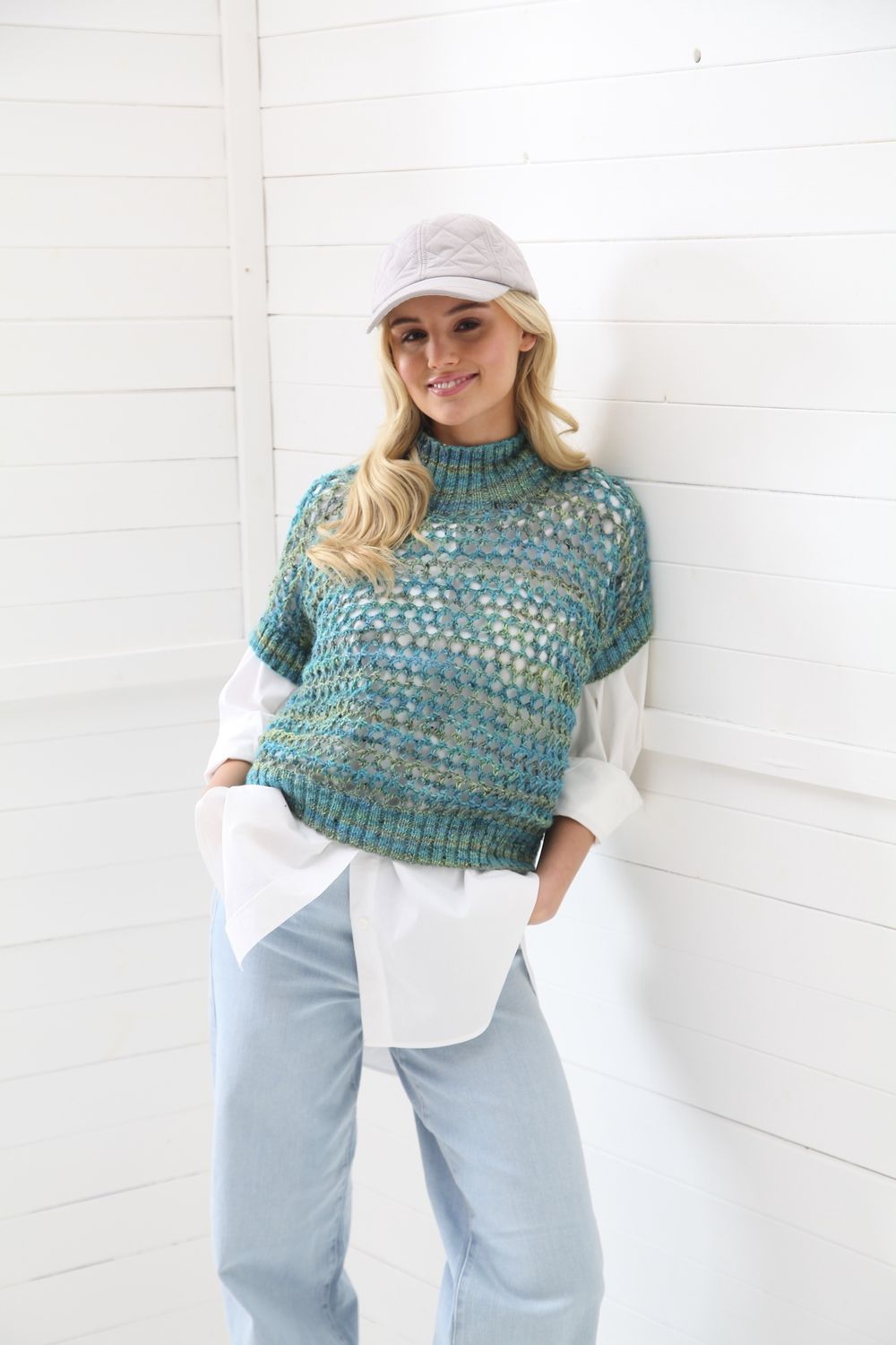 A woman is wearing an open-knit top in variegated blues and greens.