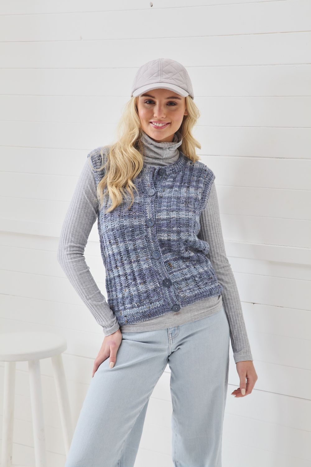 A woman is wearing a knitted waistcoat in a variegated blue and grey yarn.