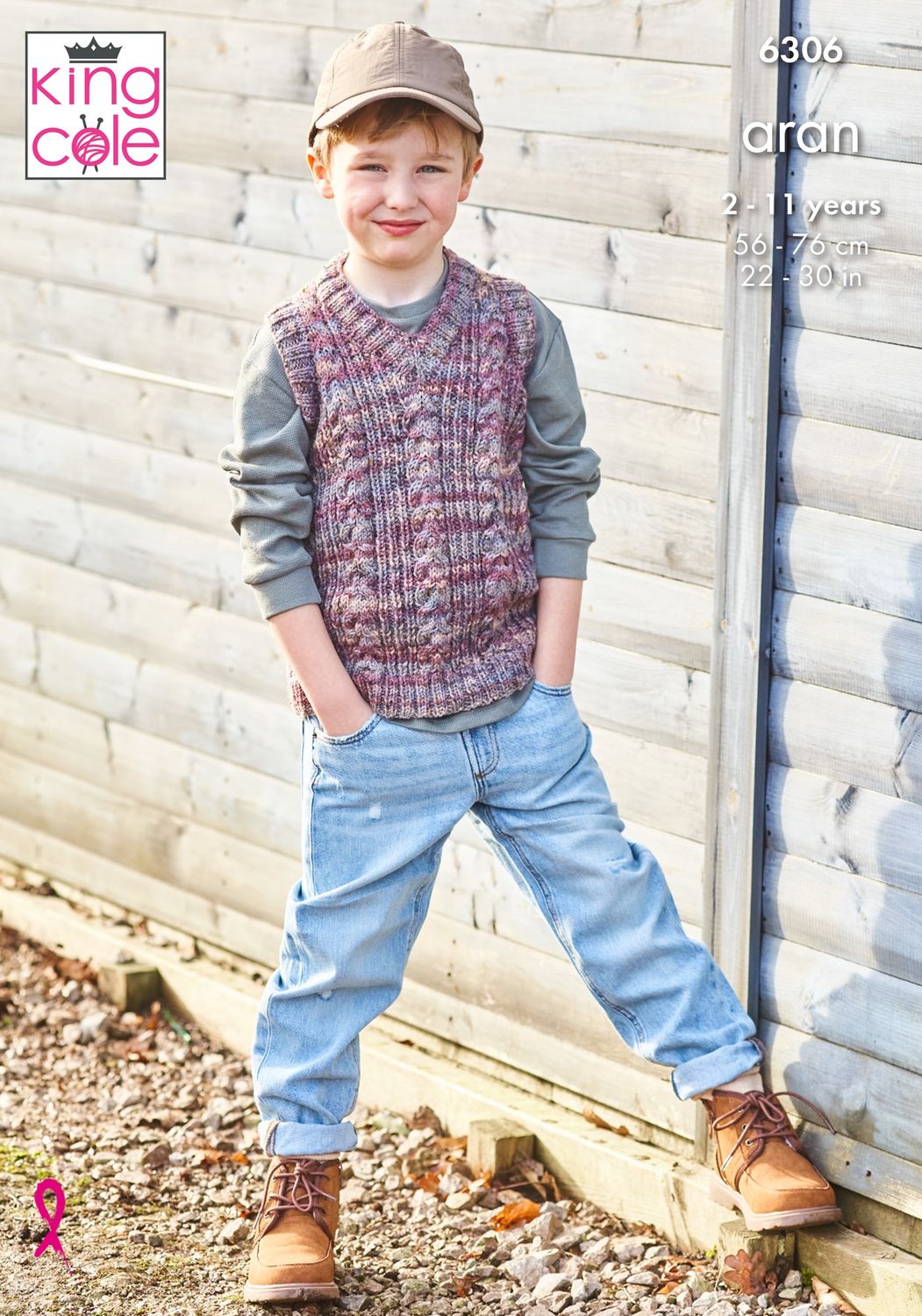 A boy is wearing a cable knit tank top in a variegated red-purple yarn.