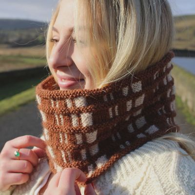 A woman is wearing a brown and cream checked effect knitted cowl.