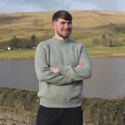 A man is wearing a light grey knitted sweater.