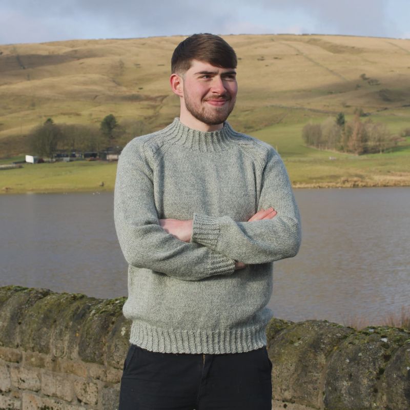 A man is wearing a light grey knitted sweater.