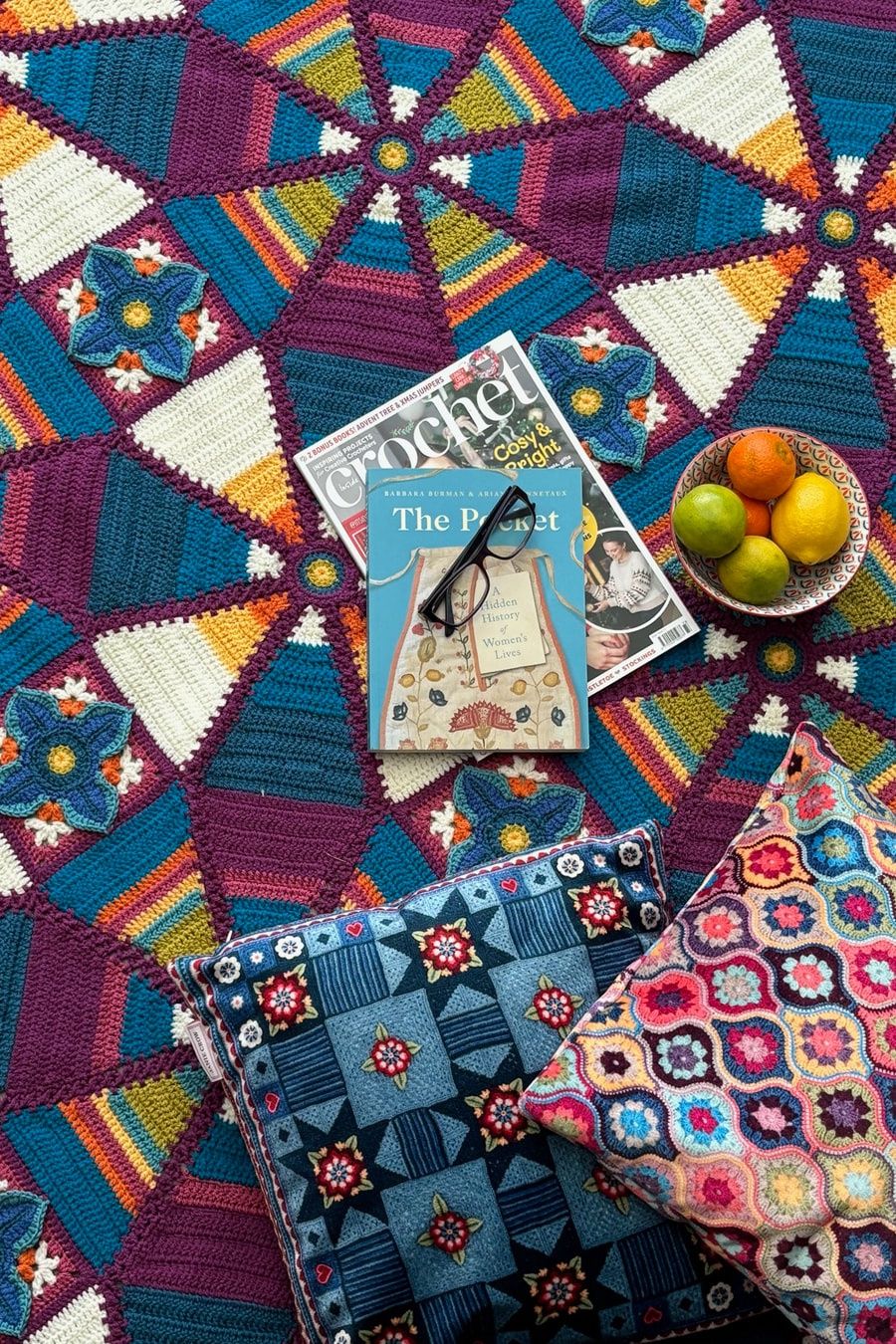 A crocheted blanket made up of squares and triangles in blues, reds and cream.