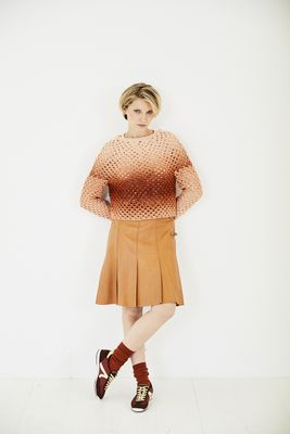 A woman is wearing a crocheted sweater in shades of burnt orange.