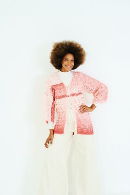A woman is wearing a crocheted jacket in shades of pink.