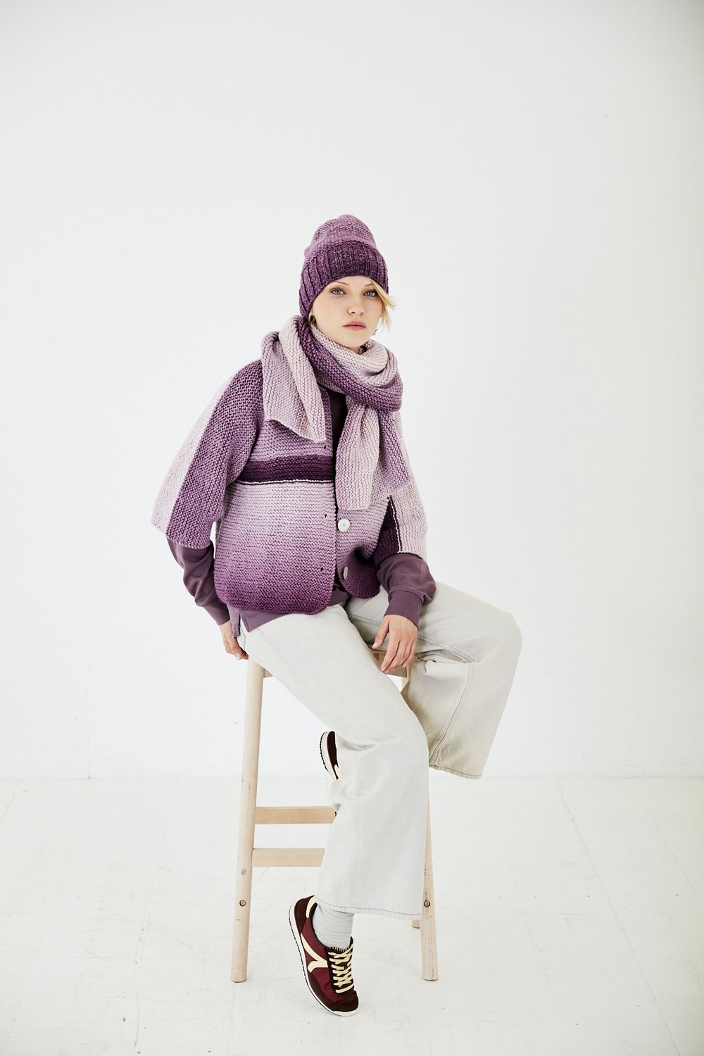 A woman is wearing a variegated purple knitted cardigan with matching hat and scarf.