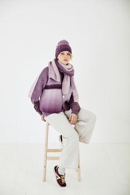 A woman is wearing a variegated purple knitted cardigan with matching hat and scarf.