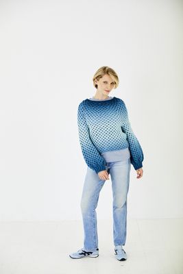 A woman is wearing a crocheted sweater in shades of blue.