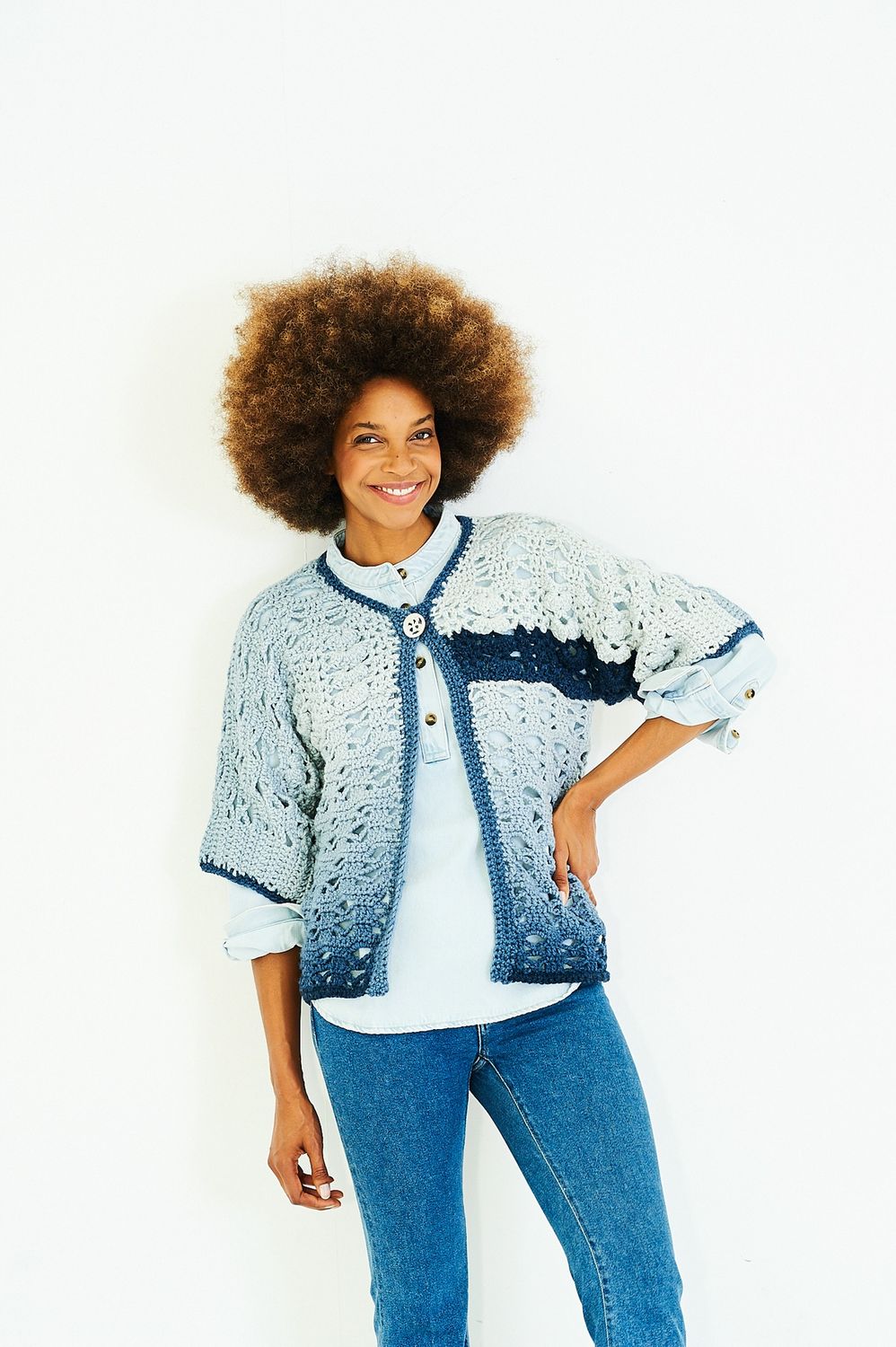 A woman is wearing a crocheted jacket in shades of blue.