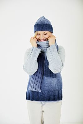 A woman is wearing a knitted sweater in a blue gradient yarn with matching hat and scarf.