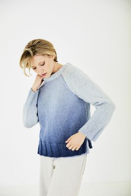 A woman is wearing a knitted sweater in a blue gradient yarn.