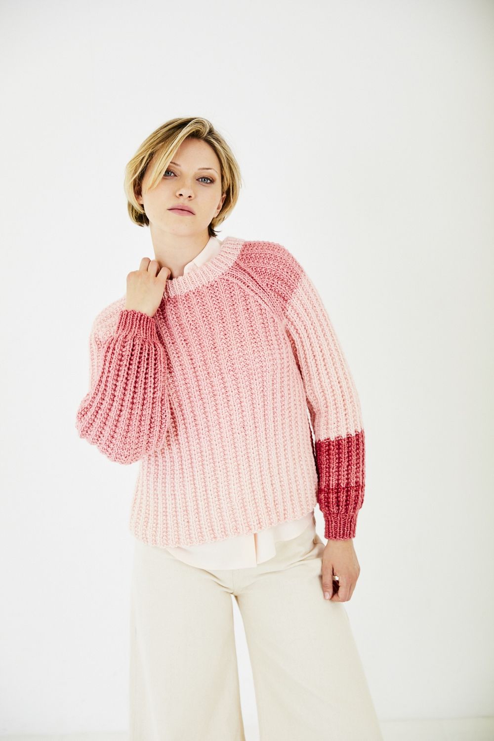 A woman is wearing a knitted sweater in a pink gradient yarn.