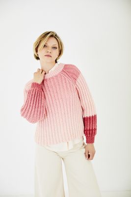 A woman is wearing a knitted sweater in a pink gradient yarn.