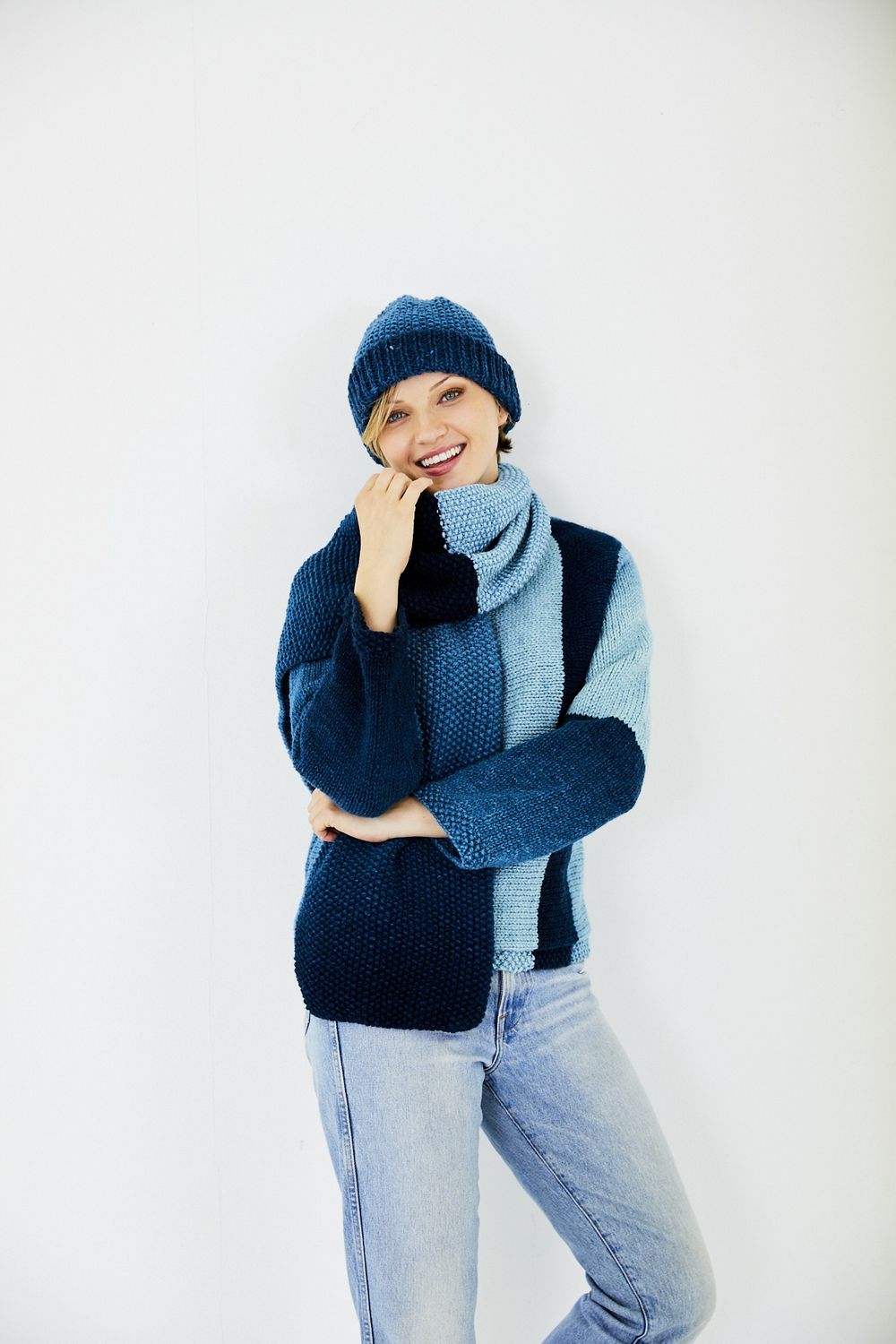 A woman is wearing a variegated blue knitted sweater with matching hat and scarf.