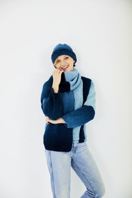 A woman is wearing a variegated blue knitted sweater with matching hat and scarf.