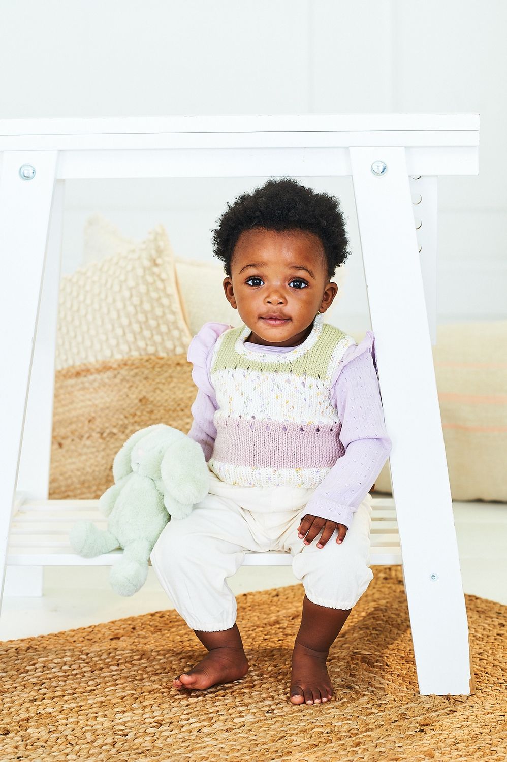 A baby is wearing a knitted tank top in green, white and purple stripes.