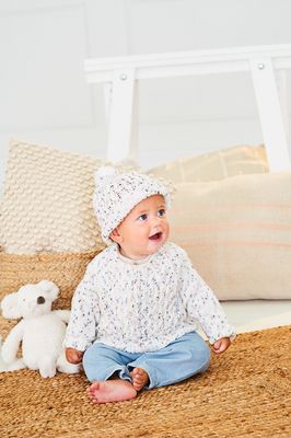 A baby is wearing a knitted sweater and hat in a white yarn with colourful speckles.