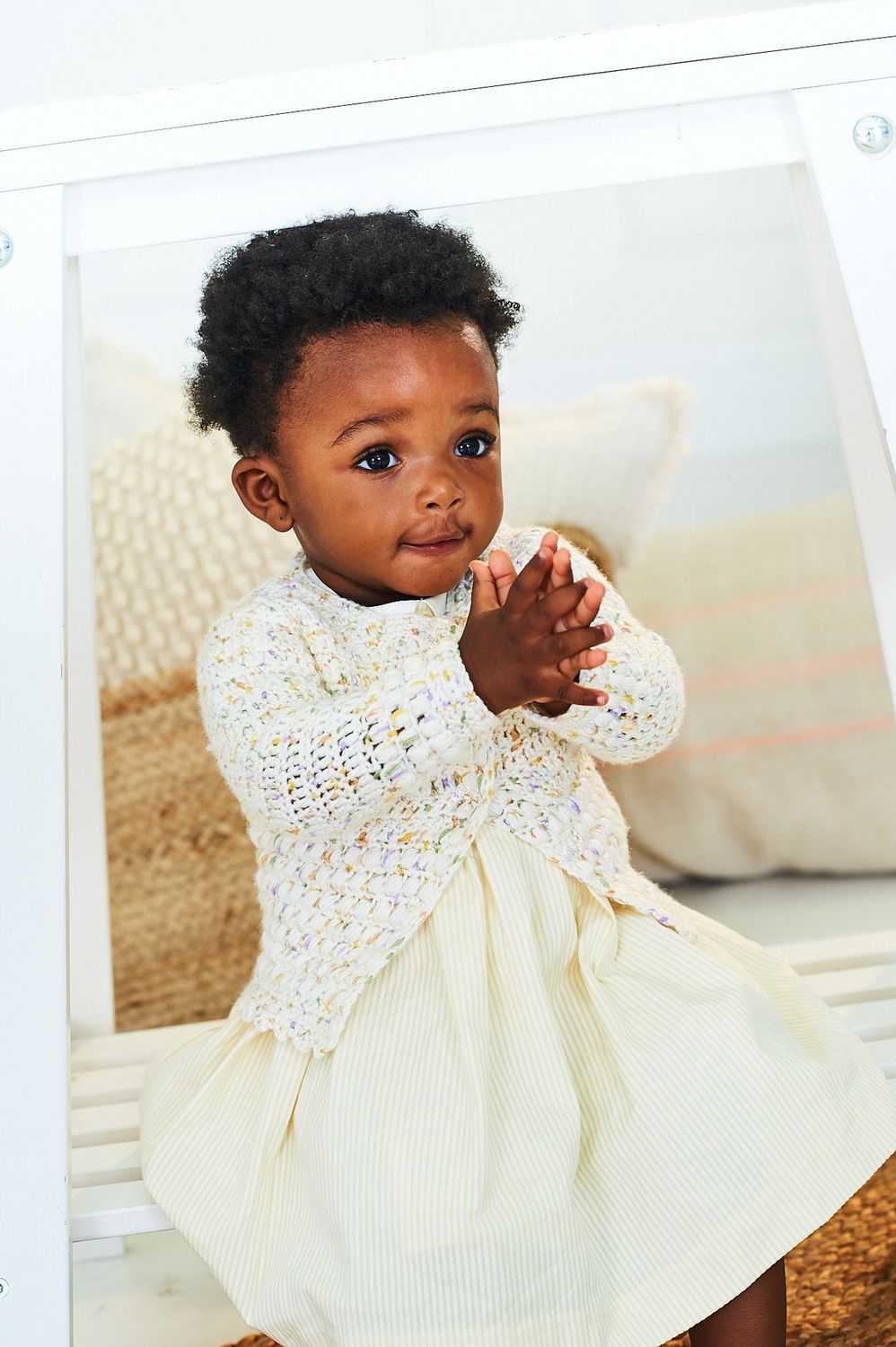 A baby is wearing a cream crocheted cardigan.